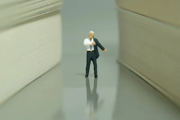 Miniature tiny people toy figure photography. A businessman getting ready wearing walking at book hallway. Grey background. Image photo