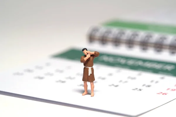 Miniature tiny people toy figure photography. A man wearing bathrobe getting shaving his beard standing above calendar. Isolated on white background. Image photo