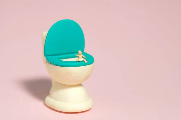 Miniature tiny people toy figure photography. A boy infant toddler whimpering, seat above potty toilet closet. Isolated on pink background. Image photo