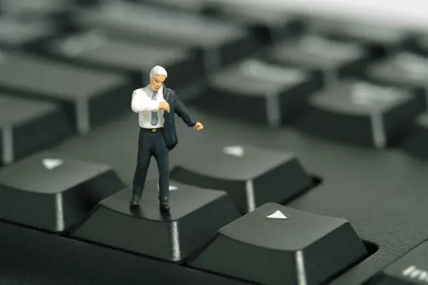 Miniature tiny people toy figure photography. A businessman getting ready wearing suit standing above keyboard. Isolated on white background. Image photo