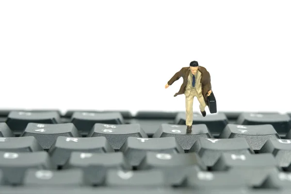 Miniature tiny people toy figure photography. A businessman running above black keyboard carrying briefcase. Isolated on white background. Image photo