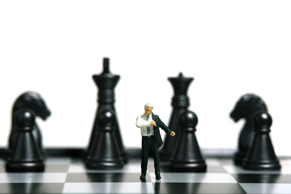 Miniature tiny people toy figure photography. Business preparation concept. A businessman getting ready wearing suit standing in front of chess pawn above chessboard. Isolated on a white background