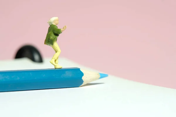 Miniature tiny people toy figure photography. A college student running above pencil carrying bag. Isolated on pink background. Image photo