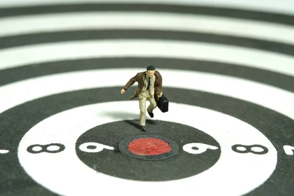 Miniature tiny people toy figure photography. A businessman running on dartboard carrying briefcase suitcase. Isolated on white background. Image photo