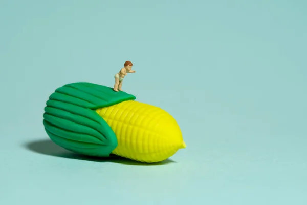 Miniature tiny people toy figure photography. Healthy food. A boy toddler infant feels happy looking at corn. Isolated on blue background. Image photo