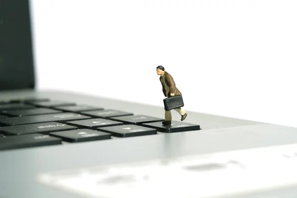 Miniature tiny people toy figure photography. A businessman running above keyboard notebook laptop carrying briefcase. Isolated on white background. Image photo