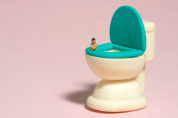 Miniature tiny people toy figure photography. A girl infant toddler seat above potty toilet closet. Isolated on pink background. Image photo