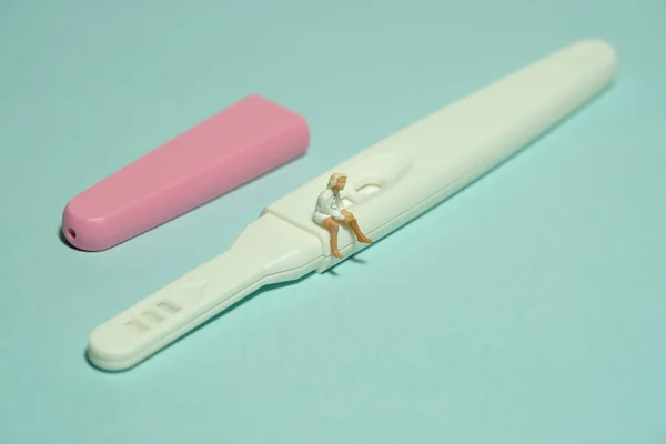 Miniature tiny people toy figure photography. A girl teenager sitting above pregnancy test pack tool. Isolated on a green background. Image photo