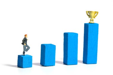 Minyatür insanlar oyuncak fotoğrafçılık. Tahta merdiveni kupayla yükselten bir öğrenci. Beyaz bir arka planda izole edilmiş. Resim fotoğrafı.