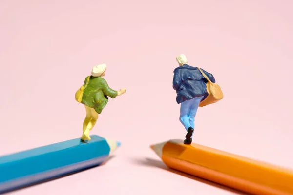 Miniature tiny people toy figure photography. Two college students running together above pencil. Isolated on pink background. Image photo