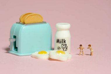 Minyatür minyatür insanlar oyuncak figürlü fotoğrafçılık. Kahvaltı yemeğinin yanında duran iki yeni yürümeye başlayan bebek. Pembe arka planda izole edilmiş. Resim fotoğrafı.