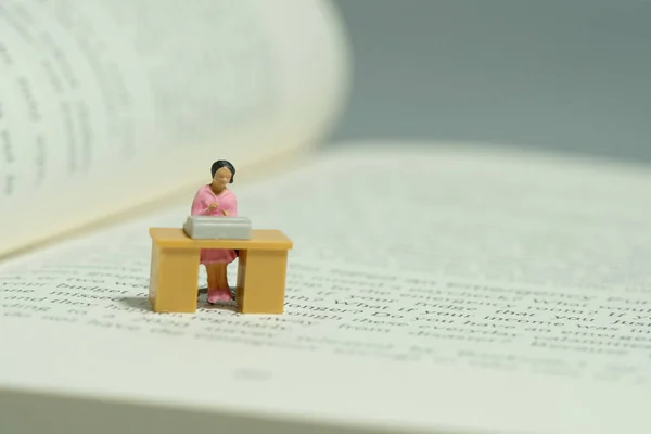 Miniature tiny people toy figure photography. Literature research. A woman seat on desk above opened book. Image photo