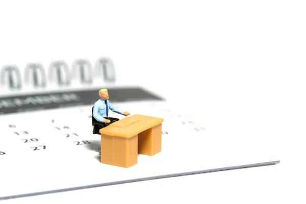 Miniature tiny people toy figure photography. Due date concept. A businessmen seat on his desk, above calendar. Isolated on a white background. Image photo