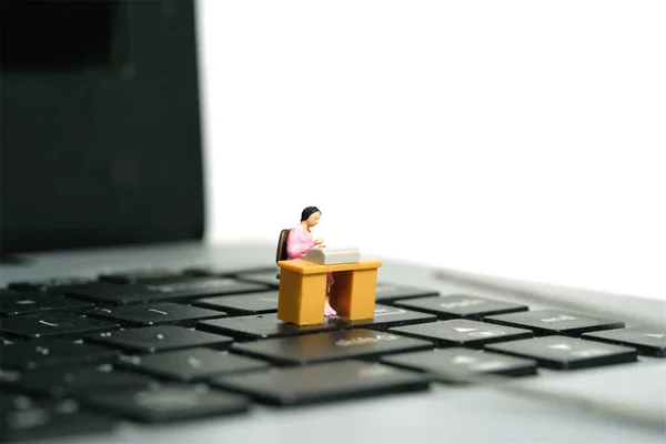 Miniature tiny people toy figure photography. A woman seat in the desk, working above notebook laptop. Isolated on a white background. Image photo
