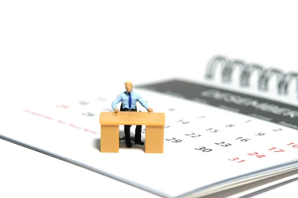 Miniature tiny people toy figure photography. Due date concept. A businessmen seat on his desk, above calendar. Isolated on a white background. Image photo