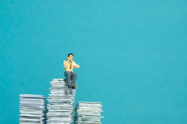 Miniature tiny people toy figure photography. Call list concept. A businessman sitting above pile of document while make a phone call. Isolated on blue background. Image photo
