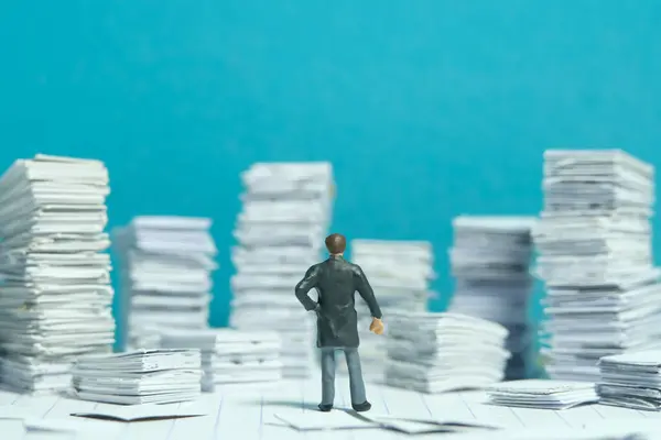 Miniature tiny people toy figure photography. File, task, work flow management plan concept. A businessman standing at a room full with pile of document. Image photo