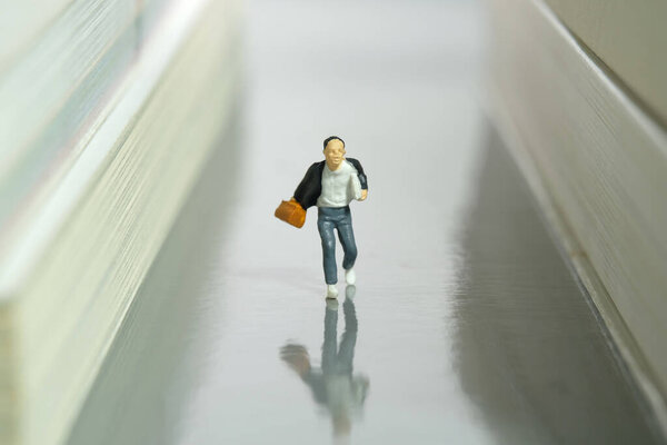 Miniature people toy figure photography. Creative concept. A boy pupil student running on a book library aisle. Image photo