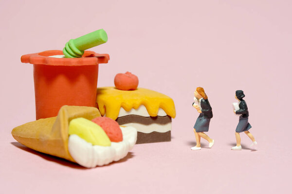 Miniature people toy figure photography. Lunch break concept. Two girl pupil students running toward cake and soft drink. Isolated on a pink background. Image photo