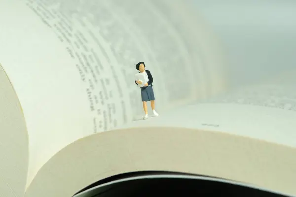 Miniature people toy figure photography. A girl pupil student running above opened book. Image photo