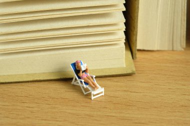 Minyatür insanlar oyuncak fotoğrafçılık. Kitap okurken plaj sandalyesinde rahatlayan bir kız. Resim fotoğrafı.
