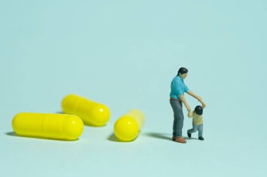 Miniature people toy figure photography. Drug medicine refuses concept. A father and son standing beside medicine pills. Isolated blue background. Image photo