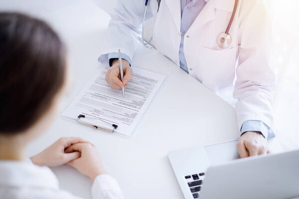 Doctor and patient discussing something and using laptop while sitting opposite each other at the desk in clinic office. Perfect medical service and medicine concept.