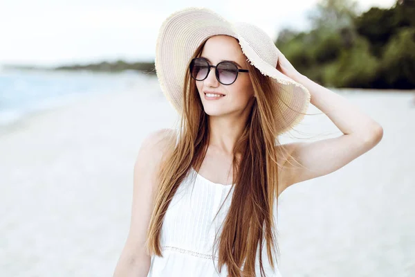 ハッピーな笑顔の女性の肖像画は 帽子とサングラスが並ぶ海のビーチで幸せに満ちています 旅行休暇中に自然を楽しむ白い夏のドレスの女性モデル — ストック写真