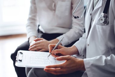 Doktor ve hasta klinikteki koltukta oturuyor. Kadın doktorların ellerinin ilaç geçmişi formunu doldurmasına odaklan, kapat. Tıp konsepti.