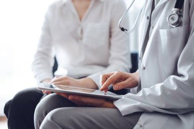 Doktor ve hasta klinikteki koltukta oturuyor. Tablet bilgisayar kullanan kadın doktorların ellerine odaklan, kapat. Mükemmel tıbbi hizmet ve tıp konsepti.