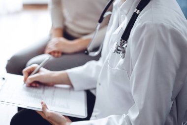 Doktor ve hasta klinikteki koltukta oturuyor. Kadın doktorların ellerinin ilaç geçmişi formunu doldurmasına odaklan, kapat. Tıp konsepti.
