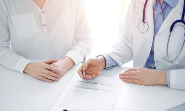 Doktor ve hasta klinikteki masada yan yana oturuyorlar. Kadın doktorların ellerinin tıbbi geçmiş kayıtlarını doldurması ya da kontrol listesi üzerinde yoğunlaşacağız. Kapat. Tıp konsepti.