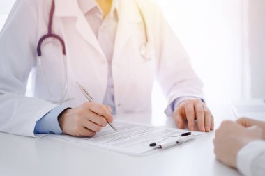 Doktor ve hasta klinikteki masada karşılıklı oturuyorlar. Kadın doktorların ellerinin tıbbi geçmiş kayıtlarını doldurması ya da kontrol listesi üzerinde yoğunlaşacağız. Kapat. Tıp konsepti.