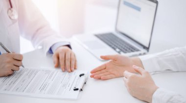 Doktor ve hasta klinikteki masada karşılıklı otururken sağlık muayenesini tartışıyorlar. Odak noktası kadın elleri, yakın çekim. Tıp konsepti.