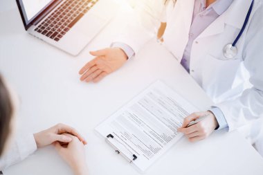 Doktor ve hasta birbirlerine karşı otururken sağlık sorularını tartışıyorlar ve klinikteki masada pano kullanıyorlar, sadece elleri yakın çekim. Tıp konsepti.