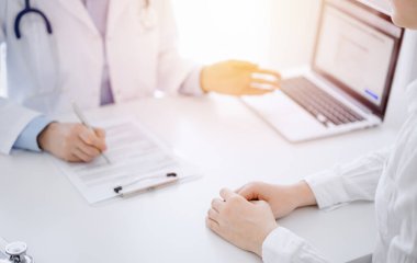 Doktor ve hasta klinikteki masada karşılıklı otururken tablet bilgisayar kullanıyorlar. Doktorun yanındaki kadın ellerine odaklan, yakın çekim. Tıp konsepti.