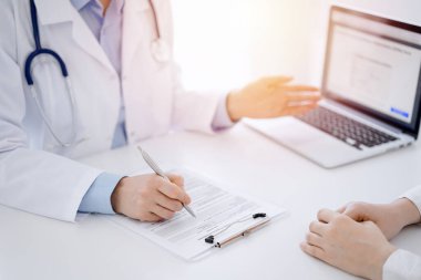 Doktor ve hasta klinikteki masada karşılıklı oturuyorlar. Kadın doktorların ellerinin tıbbi geçmiş kayıtlarını doldurması ya da kontrol listesi üzerinde yoğunlaşacağız. Kapat. Tıp konsepti.