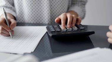 Müşteri için vergi sayarken hesap makinesi ve dizüstü bilgisayar kullanan kadın muhasebeci. İş denetimi ve finans kavramları.