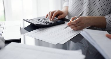 Müşteri için vergi sayarken hesap makinesi ve dizüstü bilgisayar kullanan kadın muhasebeci. İş denetimi ve finans kavramları.