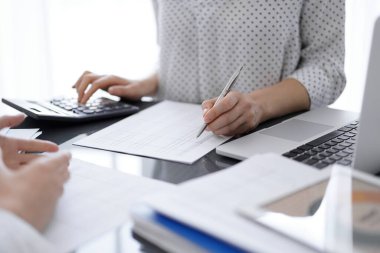 Kadın muhasebeci, hesap makinesi ve dizüstü bilgisayar kullanarak bir müşteriyle ya da meslektaşıyla vergileri sayıp tartışıyor. İş denetleme ekibi.