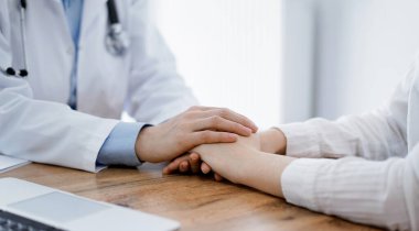 Doktor ve hasta klinikteki ahşap masada oturuyorlar. Kadın doktorların elleri güven veren kadınlarındır. Tıp konsepti.