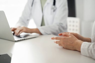 Doktor ve hasta klinikteki masada otururken sağlık muayenesini tartışıyorlar. Bilgisayarı kullanan kadın hastaların ellerine odaklan, kapat. Mükemmel tıbbi servis ve ilaç.
