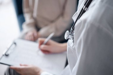 Doktor kadın ve çocuk hasta muayene odasında, steteskop yakın çekim. Pediyatrist panoya tıbbi form dolduruyor, kapat. Tıp, sağlık hizmetleri kavramları.