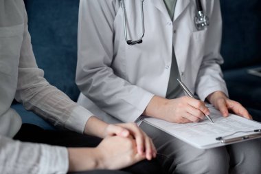 Doktor ve hasta klinikteki koltukta oturuyor. Kadın doktorların ellerinin ilaç geçmişi formunu doldurmasına odaklan, kapat. Tıp konsepti.