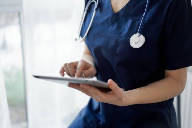 Doktor kadın panorama penceresinin yanında dururken tablet bilgisayar kullanıyor, kapatın. Doktor ya da cerrah iş başında. Tıp konsepti.