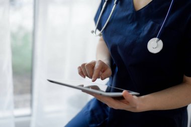 Doktor kadın panorama penceresinin yanında dururken tablet bilgisayar kullanıyor, kapatın. Doktor ya da cerrah iş başında. Tıp konsepti.