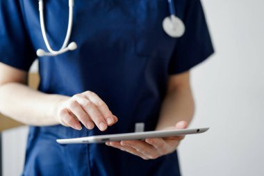 Doktor kadın panorama penceresinin yanında dururken tablet bilgisayar kullanıyor, kapatın. Doktor ya da cerrah iş başında. Tıp konsepti.