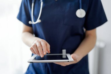 Doktor kadın panorama penceresinin yanında dururken tablet bilgisayar kullanıyor, kapatın. Doktor ya da cerrah iş başında. Tıp konsepti.