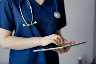 Doktor kadın panorama penceresinin yanında dururken tablet bilgisayar kullanıyor, kapatın. Doktor ya da cerrah iş başında. Tıp konsepti.