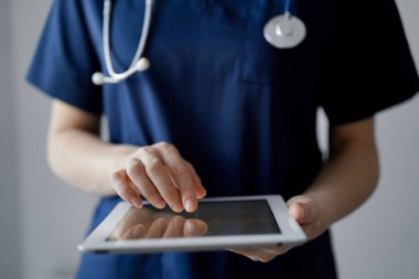 Doktor kadın panorama penceresinin yanında dururken tablet bilgisayar kullanıyor, kapatın. Doktor ya da cerrah iş başında. Tıp konsepti.